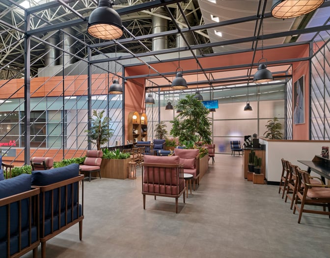 The Kepler Club lounge at Sabiha Gokcen International Airport features comfortable seating areas with tables and greenery for relaxation.