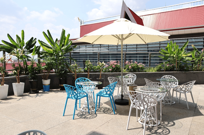 The outdoor seating area at Angkor Lounge features tables with umbrellas and chairs surrounded by potted plants at Siem Reap–Angkor International Airport.