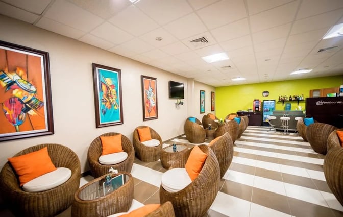 The seating area in Sala Jade at Samana El Catey International Airport features wicker chairs with cushions and a nearby bar offering beverages.