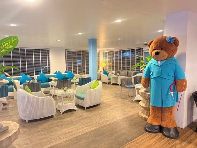 The seating area in Bangkok Airways Blue Ribbon Lounge at Samui International Airport features wicker chairs and tables with a large decorative bear.