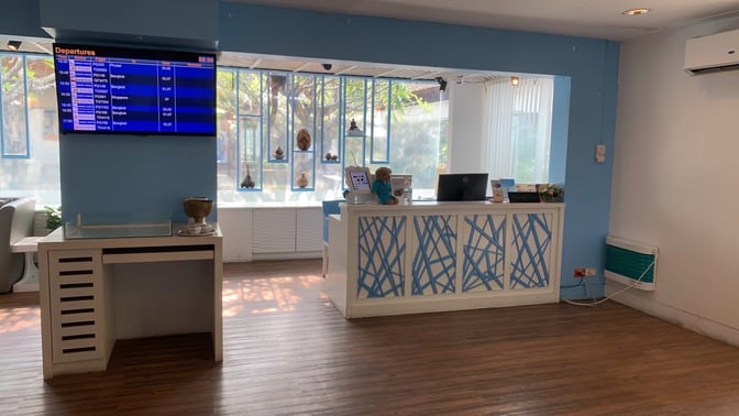 The reception area of Bangkok Airways Blue Ribbon Lounge at Samui International Airport features a check-in desk and a flight information screen.