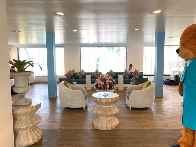 The seating area in Bangkok Airways Blue Ribbon Lounge at Samui International Airport features cushioned chairs and tables with decorative plants.