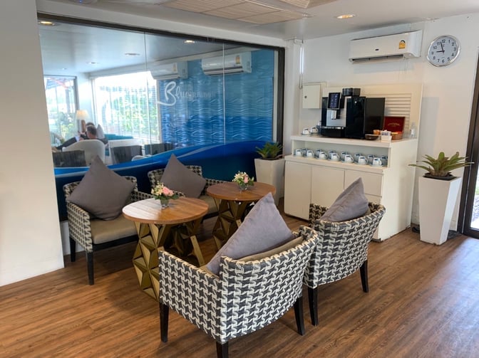 The Bangkok Airways Blue Ribbon Lounge at Samui International Airport features a seating area with cushioned chairs and a self-serve coffee station.