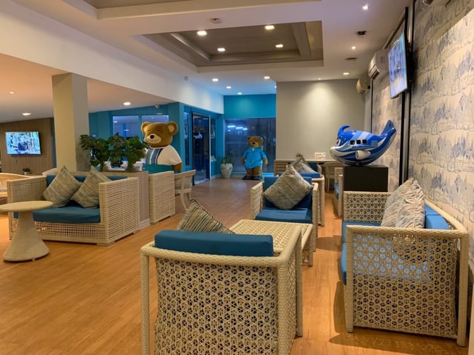 The seating area in Bangkok Airways Blue Ribbon Lounge at Samui International Airport features wicker chairs and themed decor with plush toys.