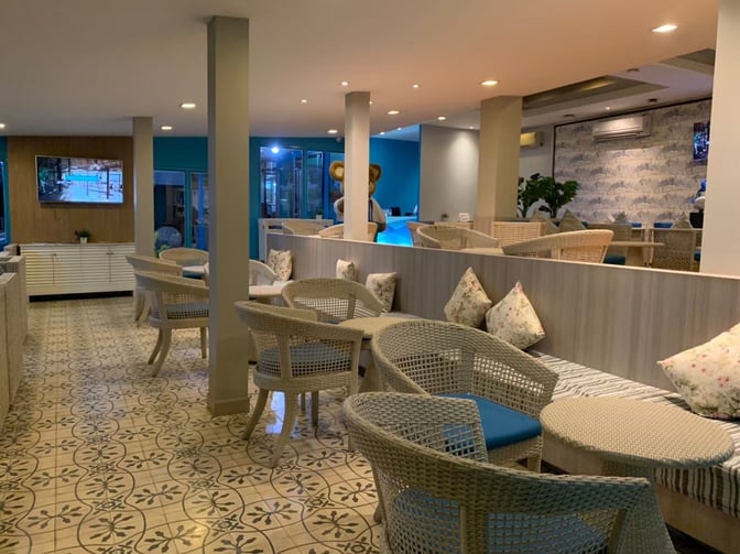 The seating area in Bangkok Airways Blue Ribbon Lounge at Samui International Airport features wicker chairs and tables with decorative cushions.