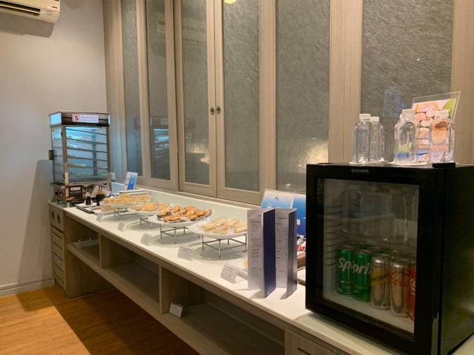The Bangkok Airways Blue Ribbon Lounge at Samui International Airport features a self-serve snack station with pastries, bottled water, and a mini fridge with beverages.