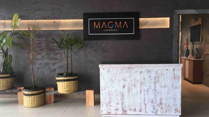 The entrance to Magma Lounge at San Cristóbal Airport features a reception desk and decorative plants, welcoming guests inside.