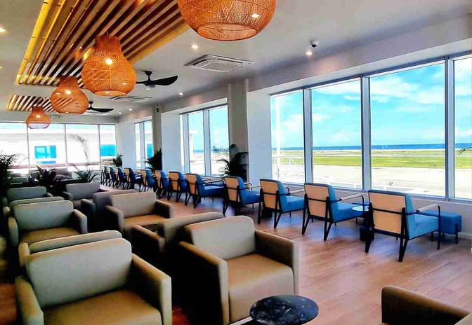 The seating area at Club Mobay Departures Lounge features armchairs and window-side chairs with views of the airport runway.