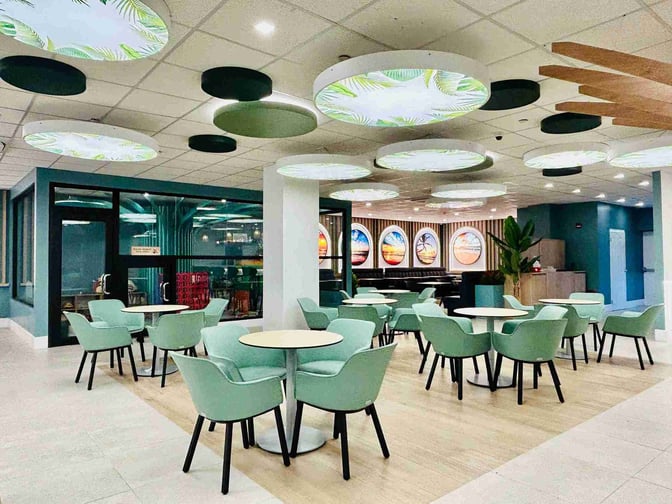 Seating area in Club Mobay Departures Lounge at Sangster International Airport features tables and chairs with decorative wall art.