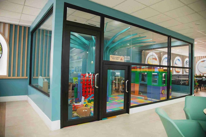 The children's play area at Club Mobay Departures Lounge features a glass-enclosed space with toys and colorful flooring.