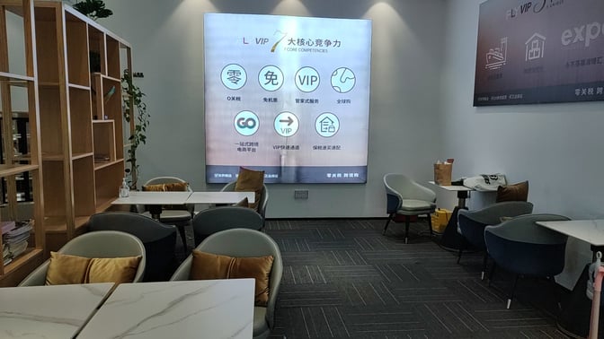 Seating area in the FLYVIP Lounge at Sanya Phoenix International Airport features tables and chairs with informational displays on the wall.