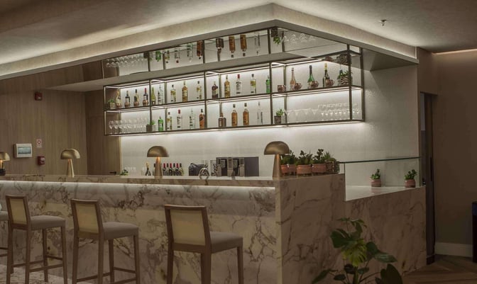 The W Lounge bar at Guarulhos Airport features a marble counter with high stools and a selection of spirits and glassware.