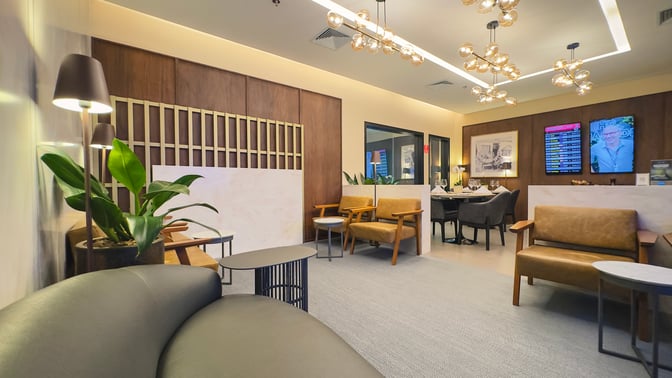 The W Lounge at Guarulhos Airport features seating areas with armchairs and tables, alongside flight information displays and dining spaces.