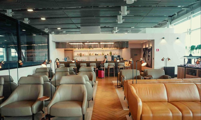 The W Premium Lounge at Guarulhos Airport features a seating area with armchairs and a bar offering various beverages.