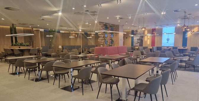 The business lounge at Sarajevo International Airport features spacious seating with tables and chairs, providing a comfortable area for travelers.