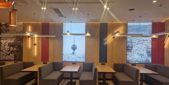 Booth seating at Sarajevo International Airport's business lounge offers semi-private dining spaces with wall art featuring local landmarks.