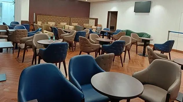 The seating area at The Lounge Terminal 2 Sardar Vallabhbhai Patel International Airport features round tables and cushioned chairs for passenger comfort.