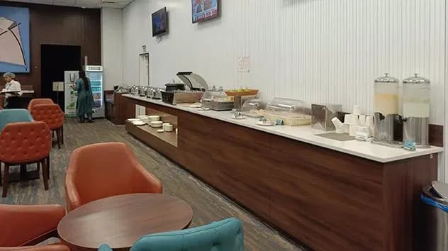 The lounge at The Lounge Terminal 2 Sardar Vallabhbhai Patel International Airport features a self-serve food station with hot and cold options and seating.