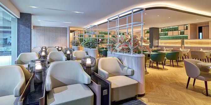 The seating area in Plaza Premium Lounge at Senai International Airport features comfortable chairs and tables, with decorative plants providing privacy.