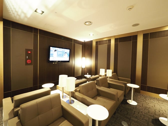 Comfortable seating with individual tables and lamps is available in the Sky Hub Lounge at Gimpo International Airport, featuring a wall-mounted TV.