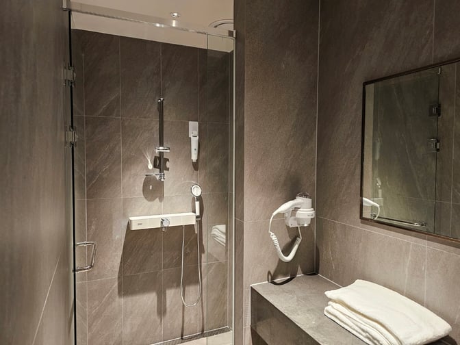 The shower facility in MATINA Lounge East at Seoul Incheon Airport includes a walk-in shower, hairdryer, and towels for guest use.