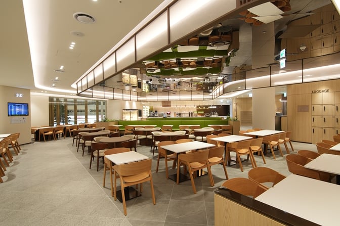 The Sky Hub Lounge East T2 at Seoul Incheon Airport features a spacious seating area with tables and chairs near a self-serve food station.