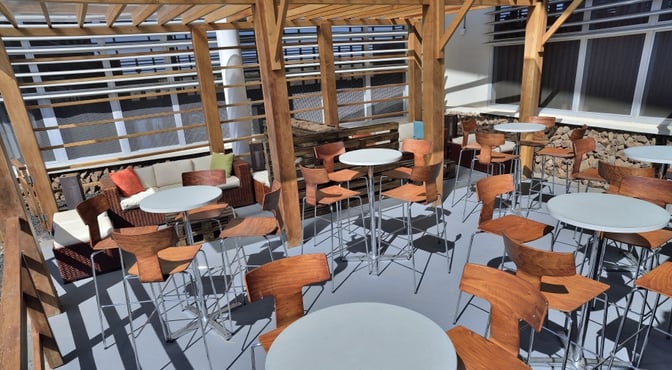 The outdoor seating area at Aeropuertos VIP Club, Seymour Airport, features round tables and wooden chairs under a pergola.