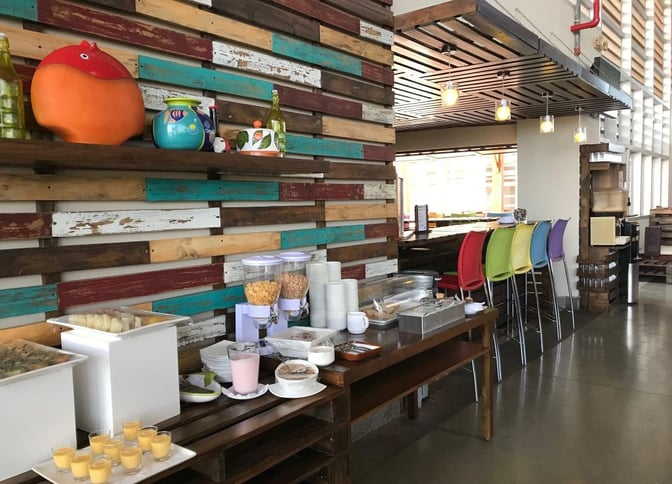 The Aeropuertos VIP Club at Seymour Airport features a self-serve breakfast station with cereals, pastries, and colorful bar seating.