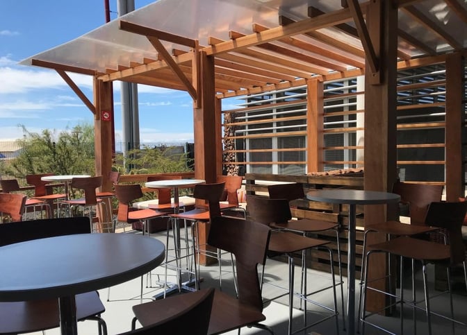 The outdoor seating area at Aeropuertos VIP Club, Seymour Airport, features tables and chairs under a wooden pergola.
