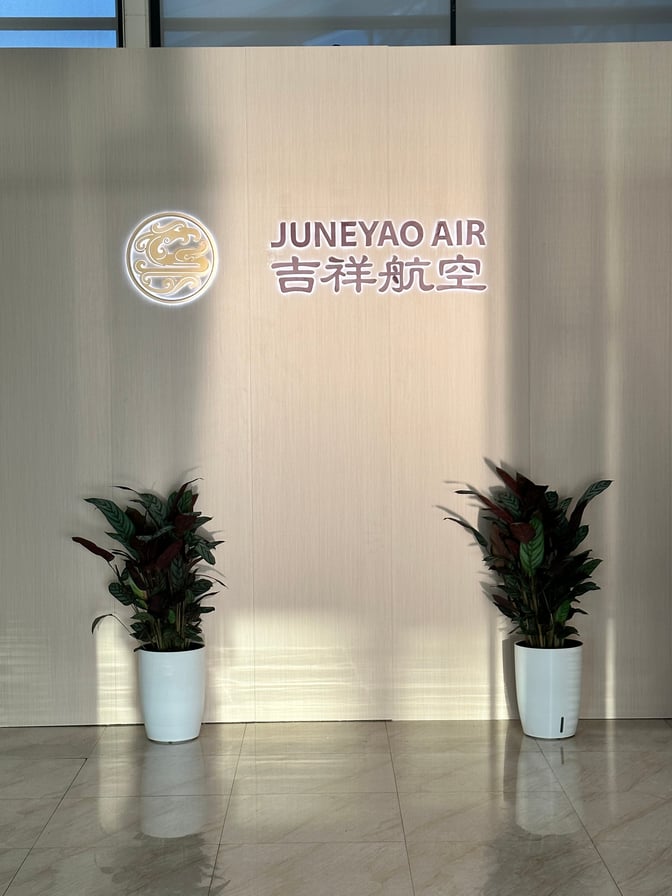 The Juneyao Air VIP Lounge entrance at Shanghai Pudong International Airport features a branded wall with decorative plants.