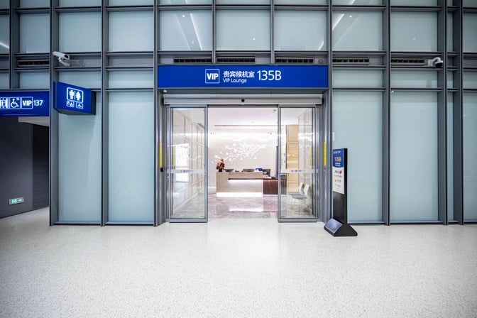 The entrance to VIP Lounge 135B at Shanghai Pudong International Airport features sliding glass doors and a reception desk inside.