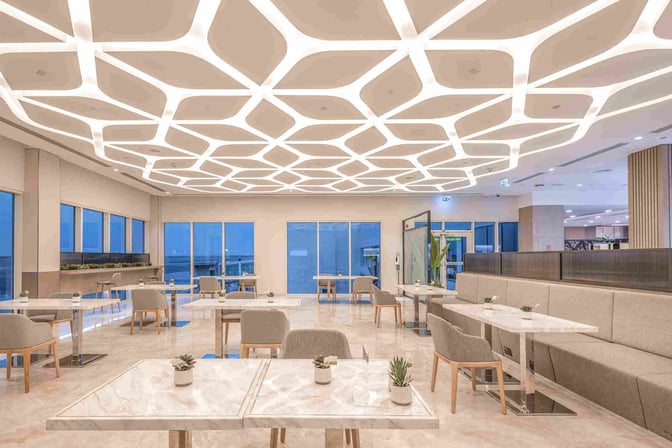 The seating area at Sharjah International Airport's lounge features tables with chairs and booth seating, offering views of the airport.