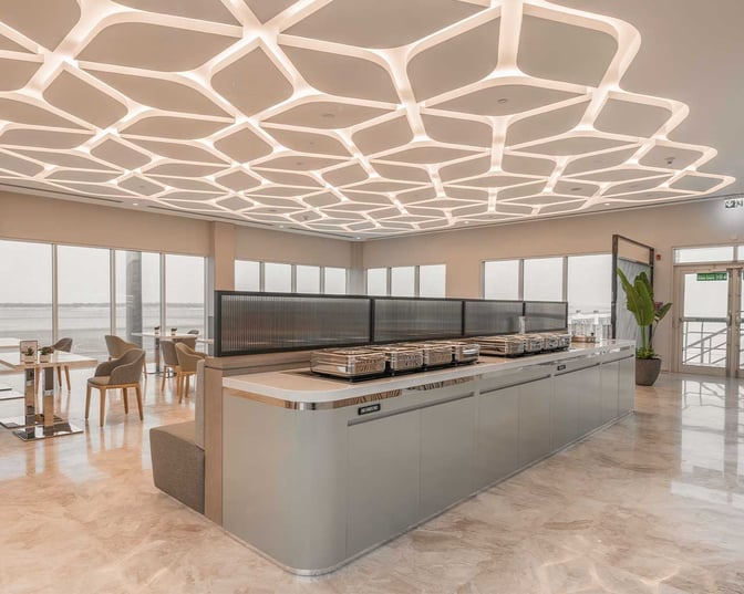 The food area at Sharjah International Airport's lounge features self-serve stations with seating offering views of the airport runway.