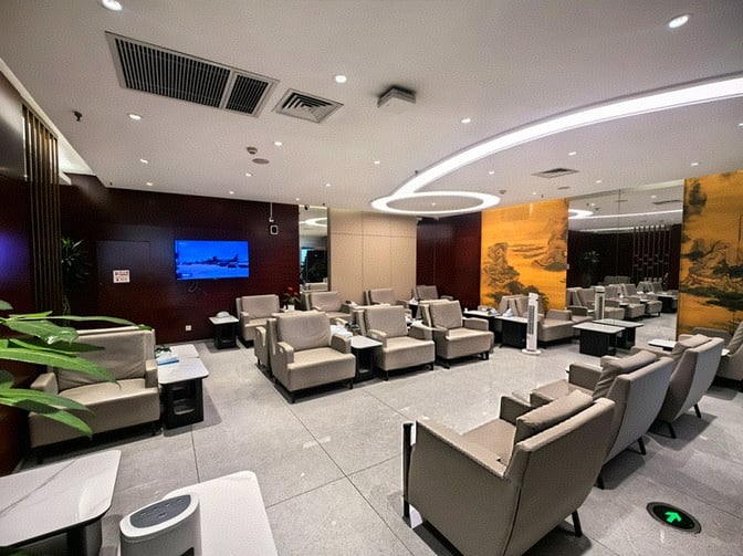 The seating area in the China Southern Lounge at Shenyang Taoxian International Airport features comfortable chairs and a wall-mounted television.
