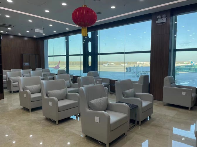 The seating area in Shenyang Taoxian International Airport's First Class Lounge offers comfortable chairs with airport runway views through large windows.