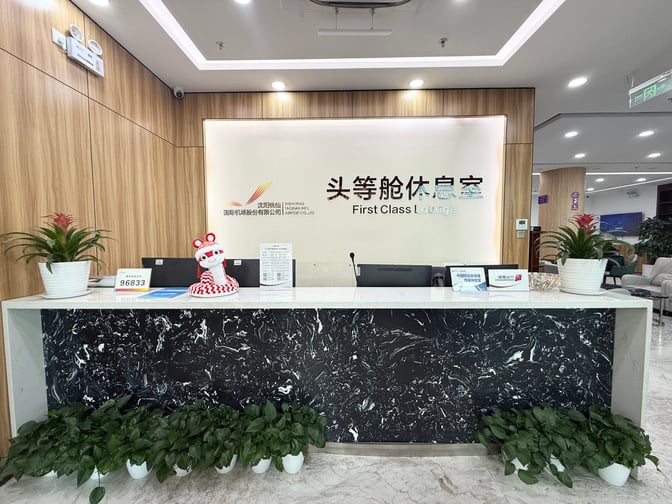 The reception desk at Shenyang Taoxian International Airport's First Class Lounge features check-in services with decorative plants and signage.