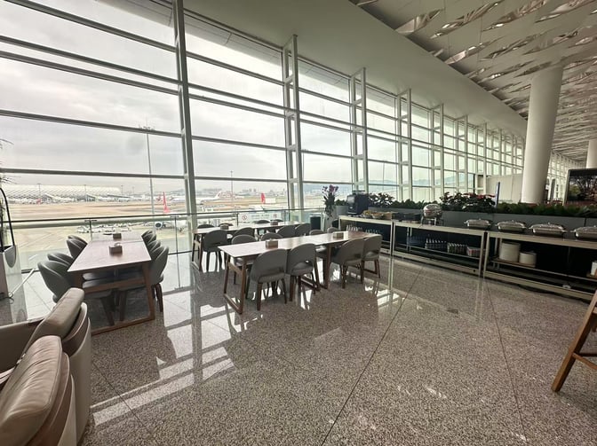 The seating area in Shenzhen Bao'an International Airport's VIP Lounge offers tables with airport views and a self-serve food station.