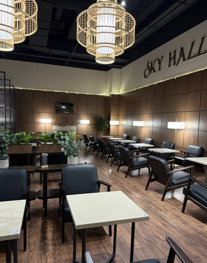 The Sky Hall Lounge at Shymkent International Airport features seating with tables, plants, and a wall-mounted television for passenger comfort.