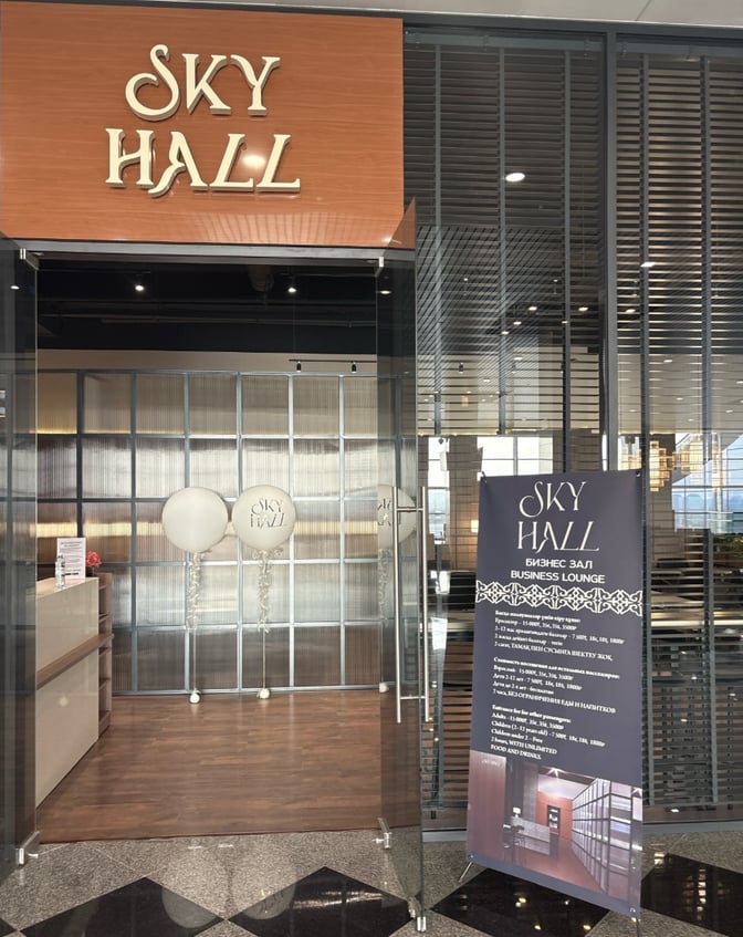 The entrance to Sky Hall Lounge at Shymkent International Airport features a reception area with informational signage and glass doors.