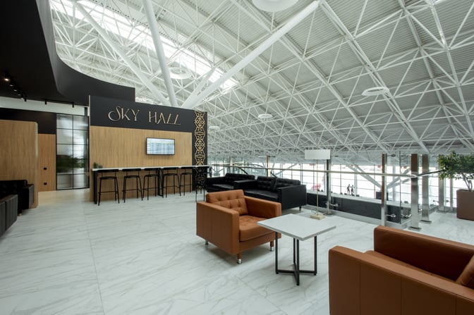 The Sky Hall Lounge at Shymkent International Airport features seating areas with armchairs and tables, and a bar with high stools.