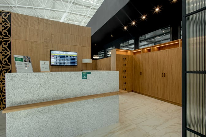 The reception area of Sky Hall Lounge at Shymkent International Airport features a check-in counter and a flight information display.