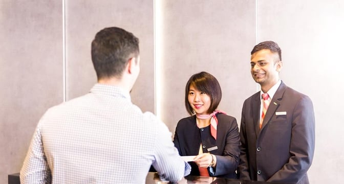 The reception area of Marhaba Lounge at Singapore Changi Airport features staff assisting a guest with check-in procedures.