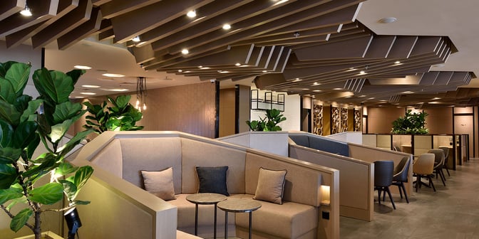 The Plaza Premium Lounge at Singapore Changi Airport features semi-private booth seating with small tables and surrounding greenery for relaxation.