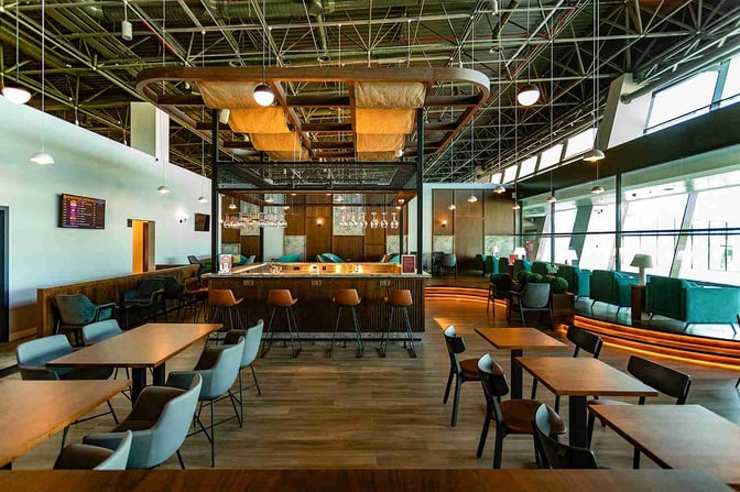 The Primeclass Lounge at Skopje International Airport features a central bar with seating, surrounded by tables and lounge chairs.