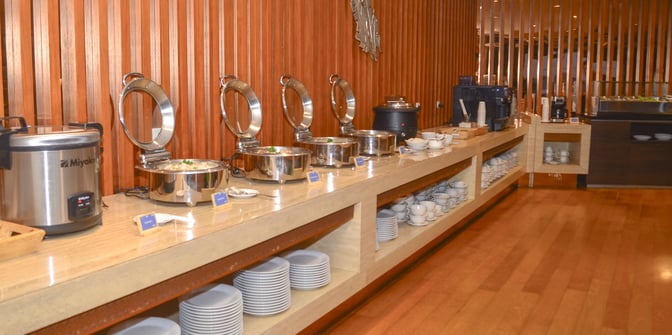The Saphire Lounge at Soekarno-Hatta International Airport features a buffet area with chafing dishes, a rice cooker, and stacked plates.
