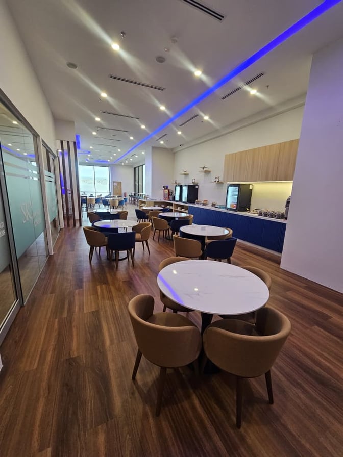 The Sky Lounge Xpress at Sultan Abdul Aziz Shah Airport features a seating area with round tables and a self-serve refreshment counter.