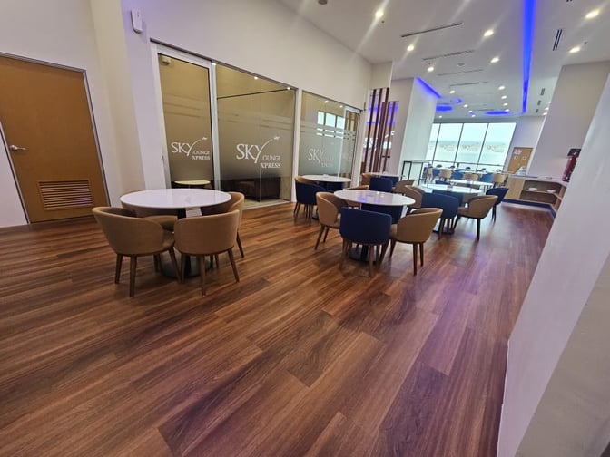 The Sky Lounge Xpress at Sultan Abdul Aziz Shah Airport features round tables with chairs, providing a comfortable seating area for travelers.