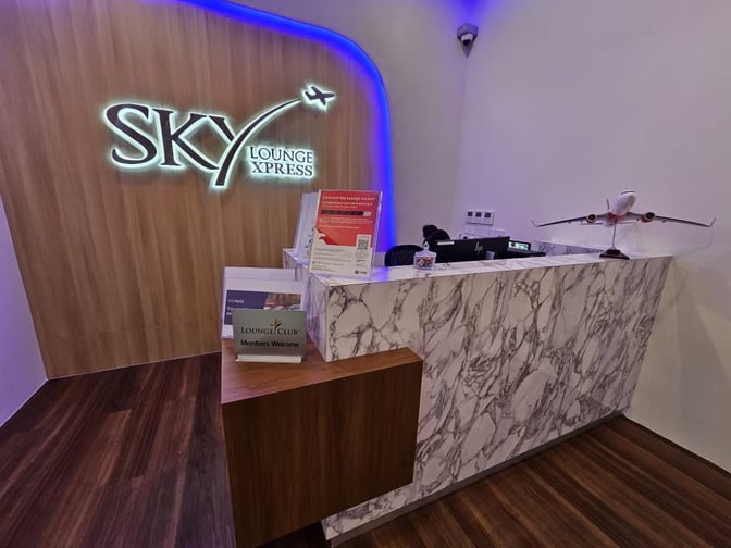 The Sky Lounge Xpress entrance at Sultan Abdul Aziz Shah Airport features a reception desk with informational brochures and a model airplane.