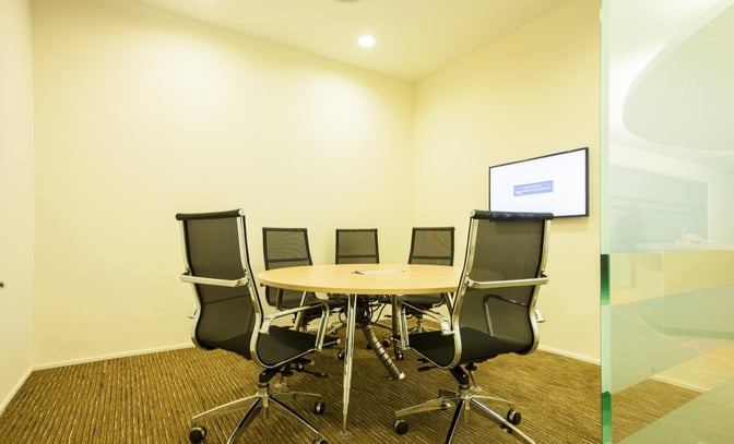 The meeting room at Sky Lounge, Sultan Abdul Aziz Shah Airport, features a round table, office chairs, and a wall-mounted screen.