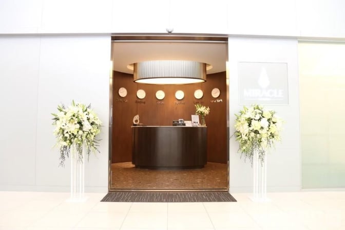 The entrance to the Miracle First and Business Class Lounge at Suvarnabhumi Airport features a reception desk and floral arrangements.